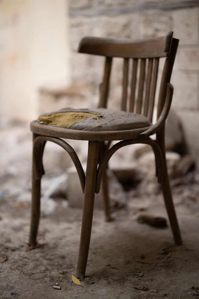 A vintage wooden chair sits in a dusty, abandoned room, creating a moody atmosphere.