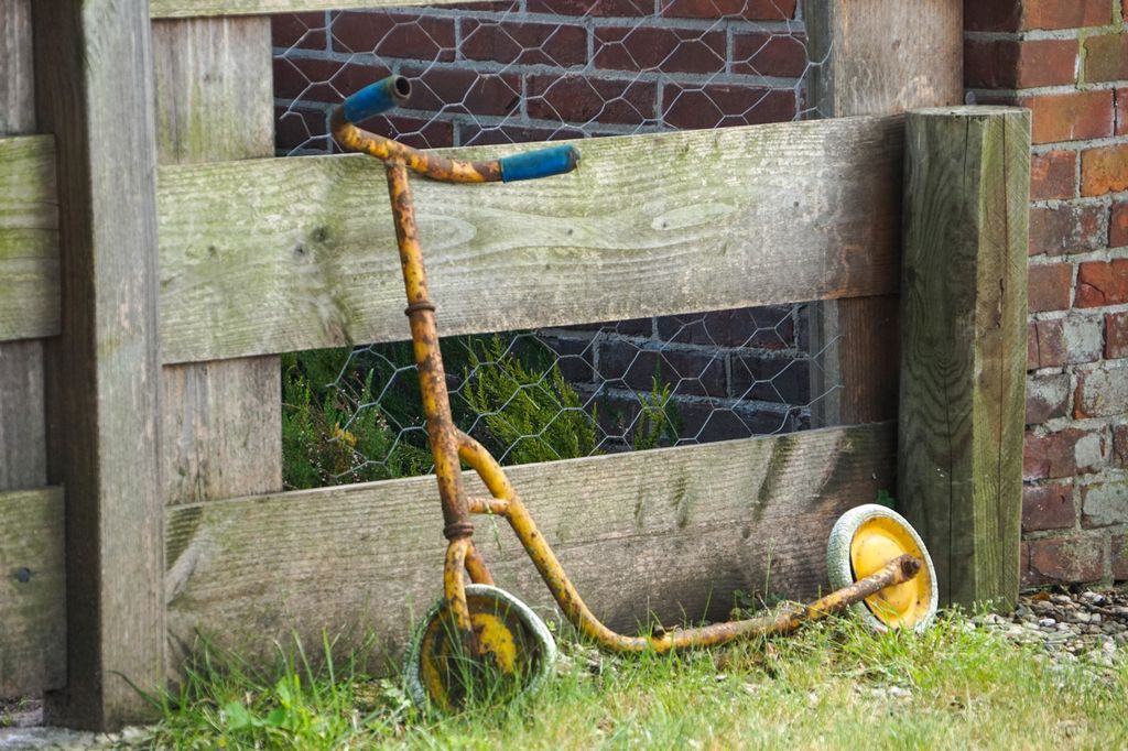 An old rusty scooter leaning against a weathered wooden fence in a rural setting.
