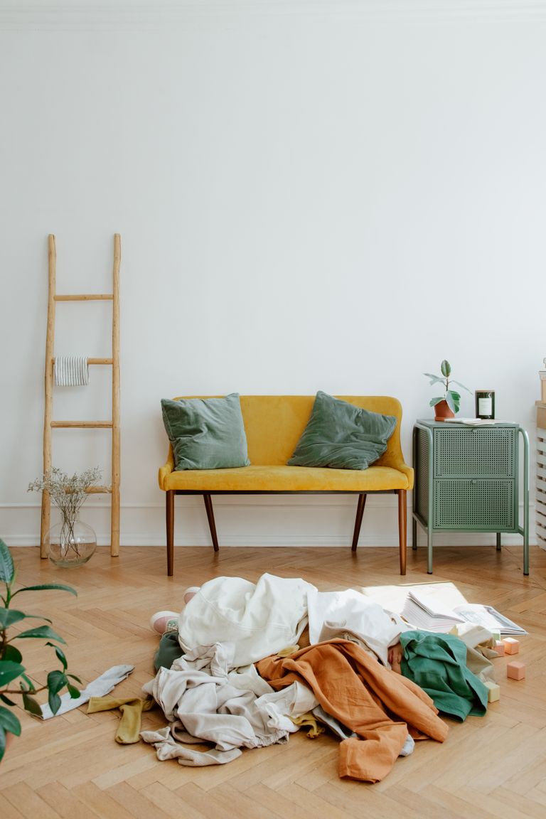 Bright and stylish living room featuring a mustard sofa, wooden ladder, and scattered clothes.